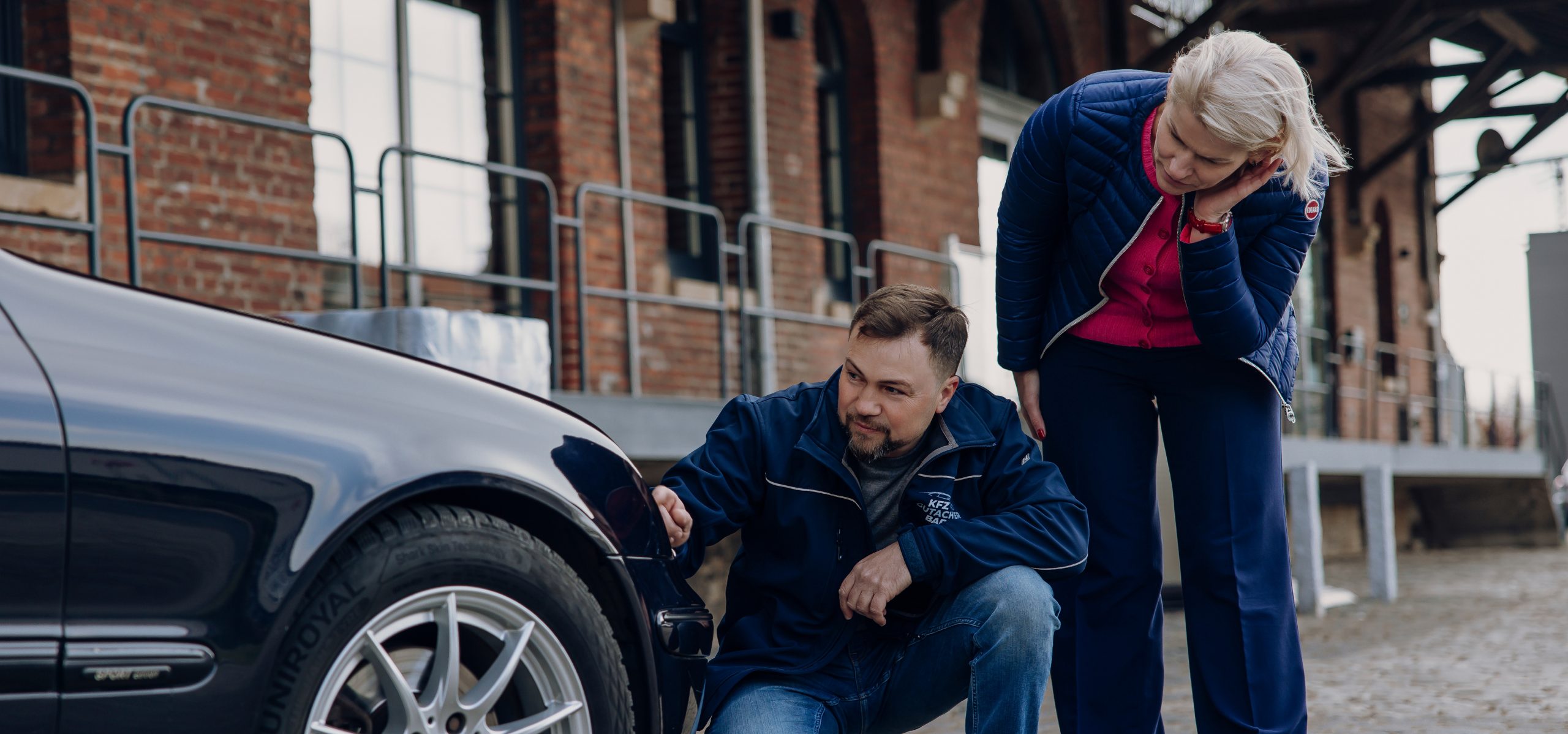 Foto von Viktor Badij mit einer Kundin vor einem Auto. Sie sehen sich den Schaden bzw. Mängel an einem Auto an.