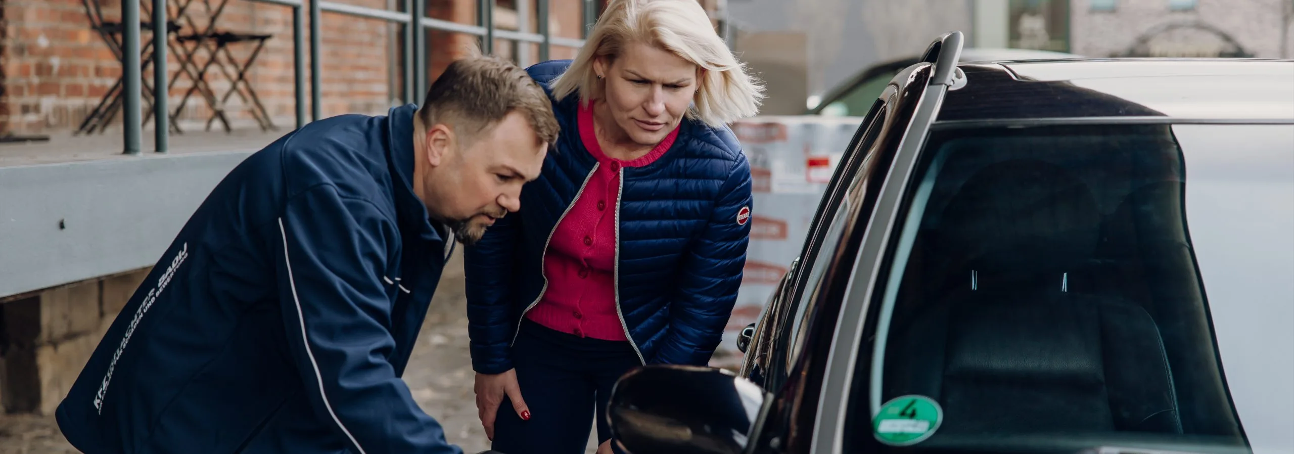 Foto von Viktor Badij mit einer Kundin vor einem Auto. Sie sehen sich den Schaden bzw. Mängel an einem Auto an.