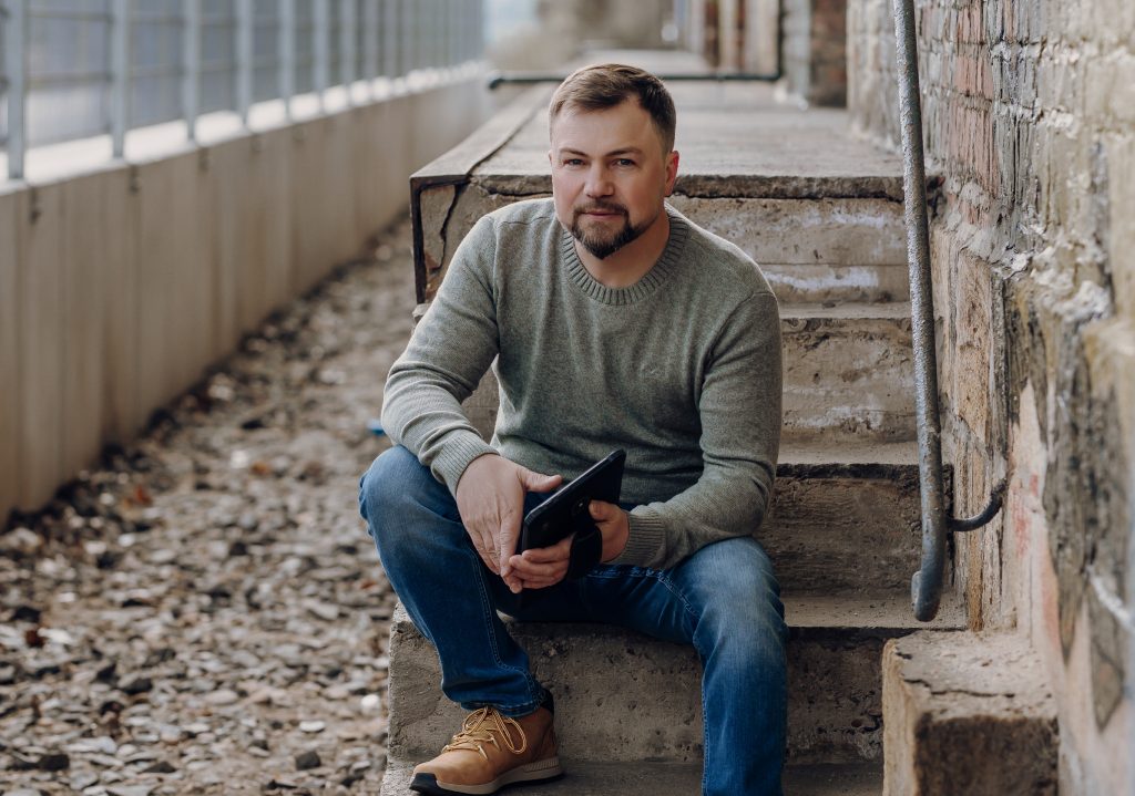 Foto von Viktor Badij mit einem Tablet in der Hand auf einer Treppe sitzend.